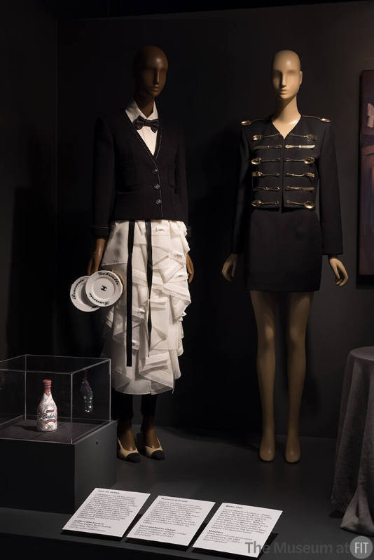 Food & Fashion Left to right: Judith Leiber Couture, Ice Champagne Bottle Bubbly minaudière, Fall 2021. Lent by Judith Leiber Couture; 2015.64.1 (waiter ensemble); 2020.6.1 (black suit)