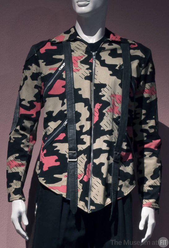 Man’s jacket in beige, pink and black camouflage print with black patches and buckled straps, d…