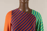 Detail view of striped color block dress showing asymmetrical neckline and left raglan sleeve h…