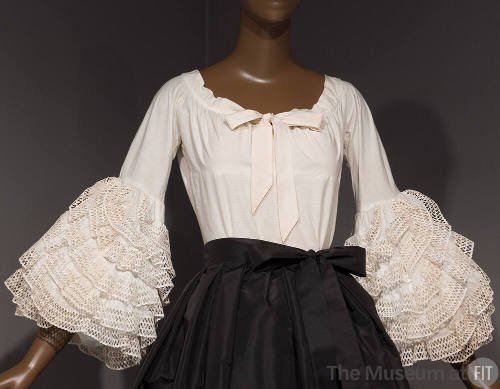 White blouse with bow at center neckline and sleeves with oversize ruffles starting at elbow