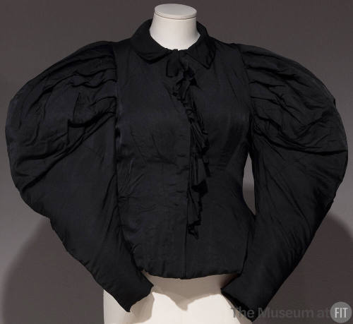 Black top with large puffy sleeves and ruffle down the center front