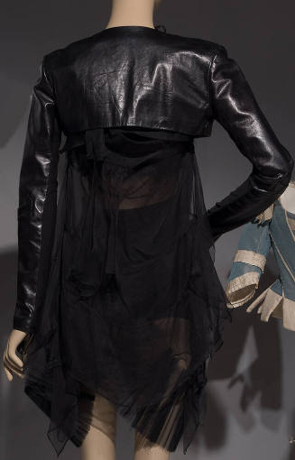 Back view of black leather cropped jacket over sheer black dress and skirt with asymmetrical dr…
