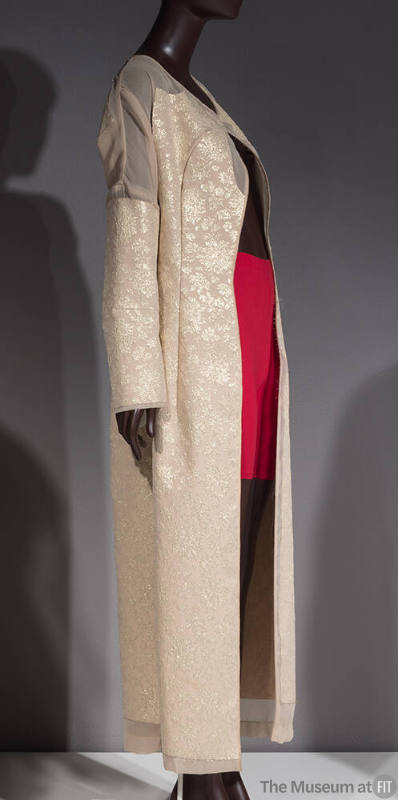 Beige floor length coat with gold floral brocade pattern and sheer insets at shoulders, cuffs a…