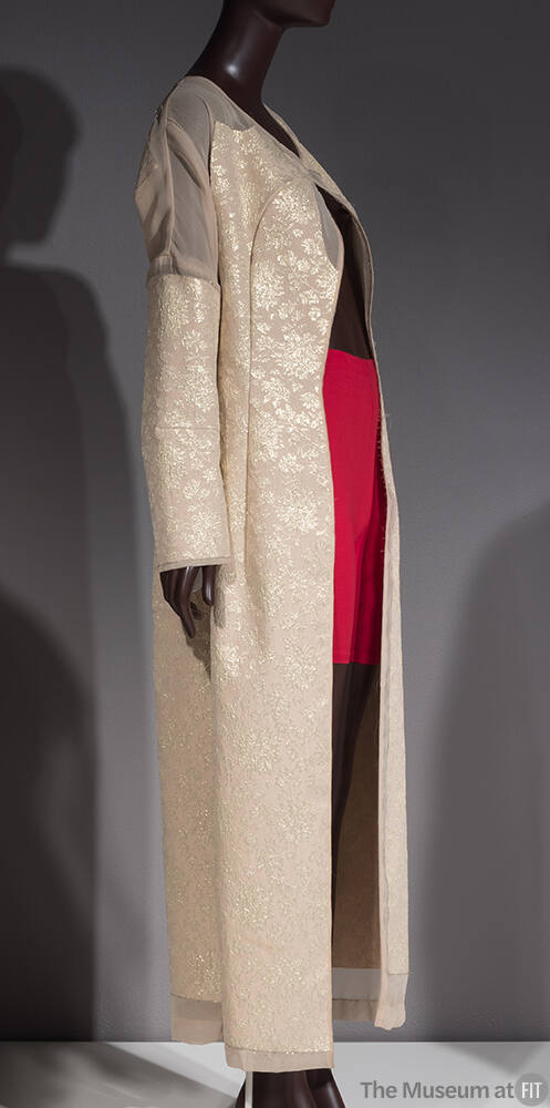 Beige floor length coat with gold floral brocade pattern and sheer insets at shoulders, cuffs a…