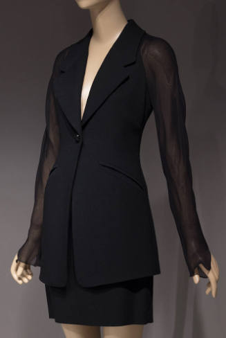 Black form fitting jacket with sheer sleeves and matching knee-length straight skirt