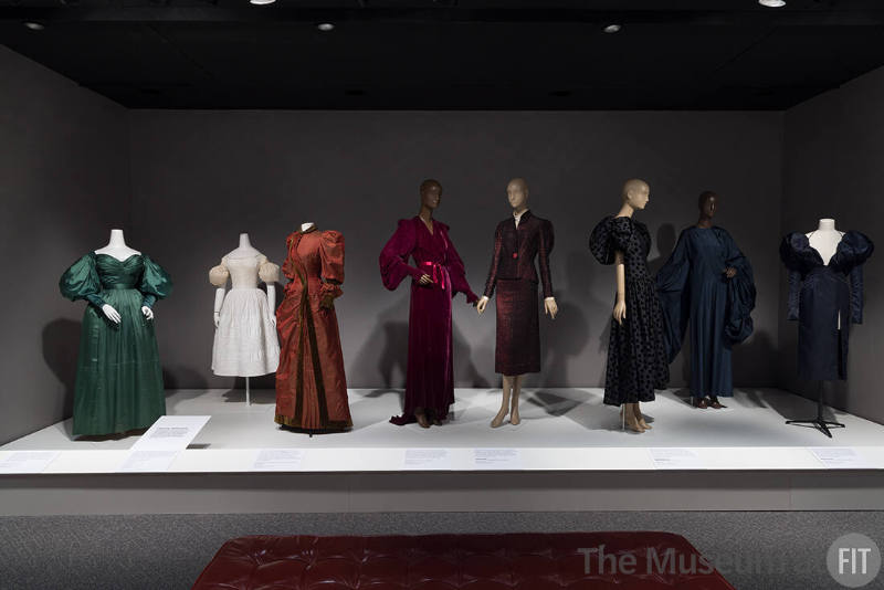 From left to right: Green dress, c.1830 (P88.28.1); sleeve puffs, c.1829 (2023.28.1); red dress, c.1895 (2019.83.1); red robe, c.1935 (2011.25.1); suit by Schiaparelli, 1935 (87.70.2); dress by Carolina Herrera, fall 1981 (88.105.13); dress by Madame Grès, c.1980 (82.234.3); dress by LaQuan Smith, spring 2022 (2023.34.1)