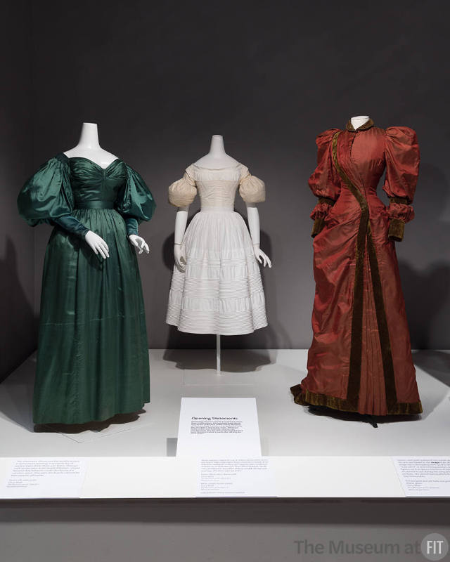 From left to right: Green dress, c.1830 (P88.28.1); sleeve puffs, c.1829 (2023.28.1); red dress, c.1895 (2019.83.1)