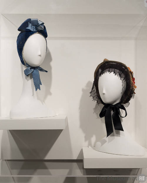 Untying the Bow exhibition installation view of a blue bonnet and black bonnet on head forms wi…