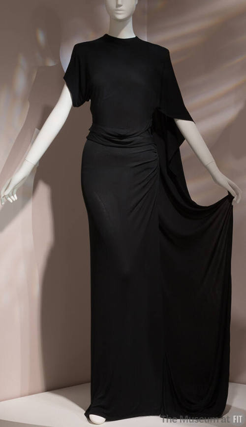 Black floor length dress with asymmetrically draped short sleeves for cape effect on left shoul…