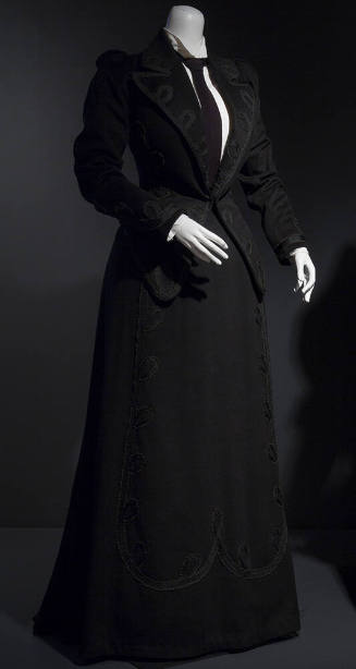 Black suit trimmed with loops of black braid on lapels, cuffs and front panel of floor length f…