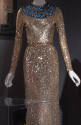 Gold sequined evening dress with long sleeves and wide jeweled collar of alternating blue and c…