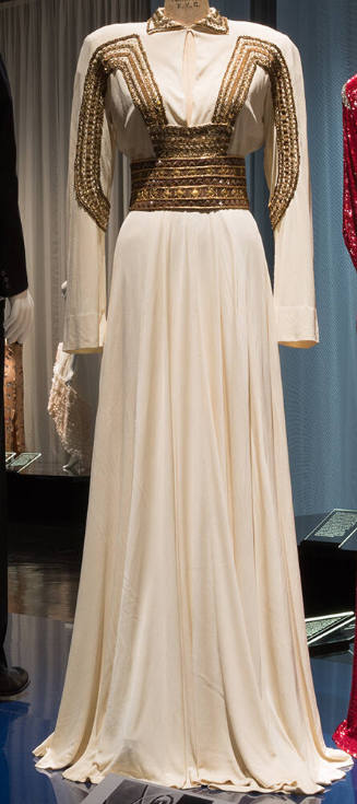 Off-white floor length evening dress with long sleeves and gold braid and square paillettes on …