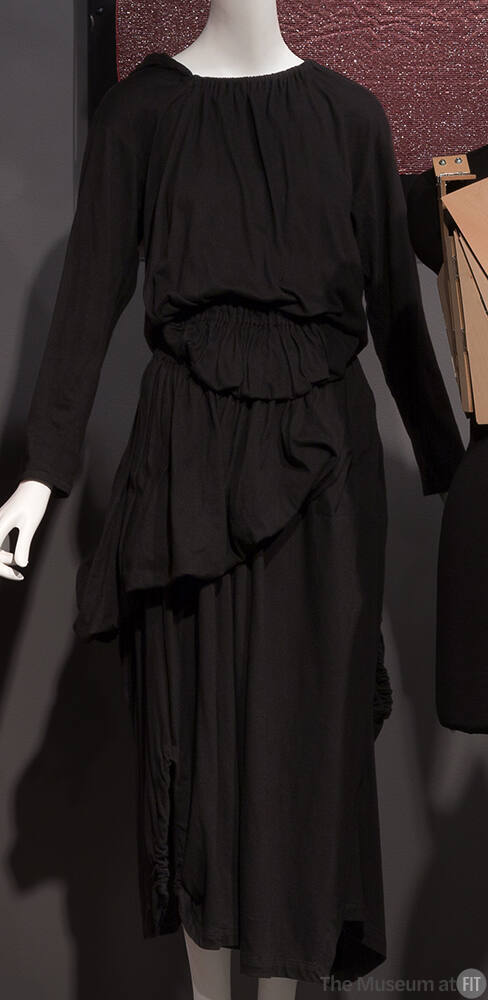 Black long sleeve dress with elasticized pouches asymmetrically draped along skirt, calf length…