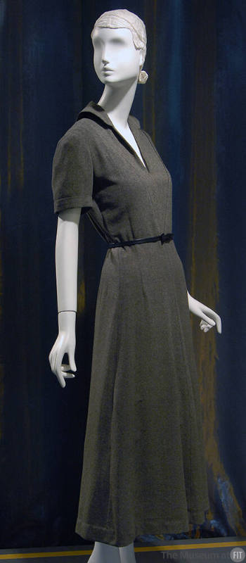 ¾ view of dark grey short sleeve ankle length dress with rounded collar, deep V-neck and slim b…