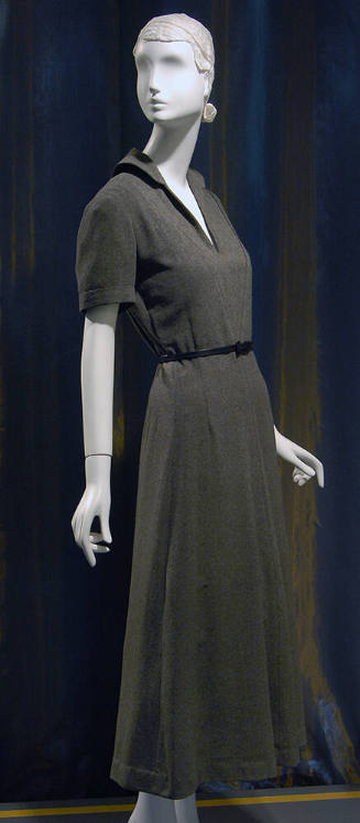 ¾ view of dark grey short sleeve ankle length dress with rounded collar, deep V-neck and slim b…