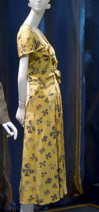 Side view of yellow dress printed with black bows with short sleeves, bodice bands tied into kn…