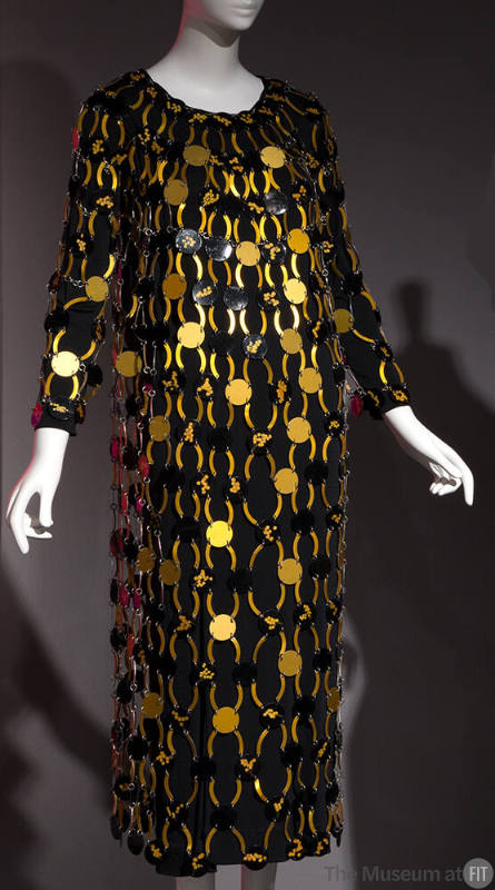 Black long sleeve calf length dress overlaid with gold and black discs connected by arched gold…