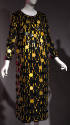 Black long sleeve calf length dress overlaid with gold and black discs connected by arched gold…