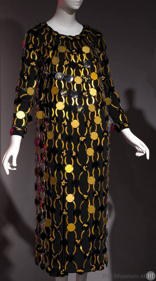 Black long sleeve calf length dress overlaid with gold and black discs connected by arched gold…