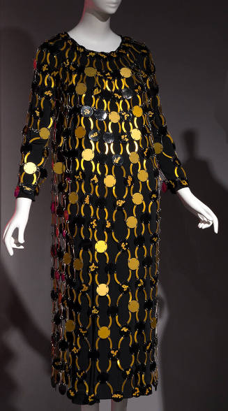 Black long sleeve calf length dress overlaid with gold and black discs connected by arched gold…