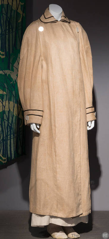 Tan long sleeve ankle length duster with black trim on spread collar and around cuffs and butto…