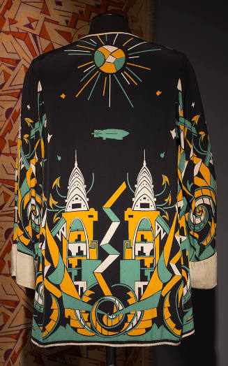 Back view of black jacket printed with Art Deco design of skyscrapers, sun and zeppelin in gold…