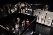 Overhead exhibition installation view of Fashioning Wonder showing dressed mannequins on cabine…