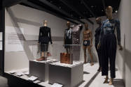 Fashioning Wonder exhibition installation view of six dressed mannequins and two cases of shoes…