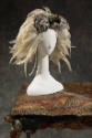 Mannequin head wearing headdress of a stuffed bird’s head amidst white feathers on top of a tab…