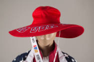 Detail view of red wide brim hat showing blue and white outlined “USA” writing around brim and …