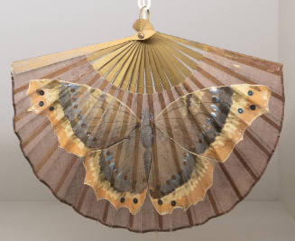 Opened brown fan with gold sticks and large painted butterfly in brown, black, blue, cream, ora…