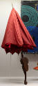 Red umbrella with miniature violin in center of wooden handle shown in front of a black textile…