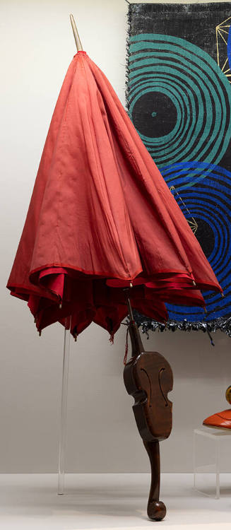 Red umbrella with miniature violin in center of wooden handle shown in front of a black textile…