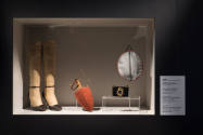 Fashioning Wonder exhibition installation view of a pair of boots, an umbrella, a cosmetics cas…