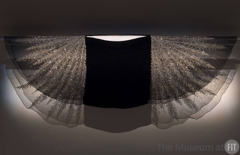 Black capelet mounted on wall with gauze sleeves extended to show crystal bead feather design a…