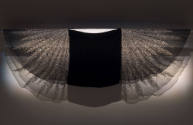 Black capelet mounted on wall with gauze sleeves extended to show crystal bead feather design a…