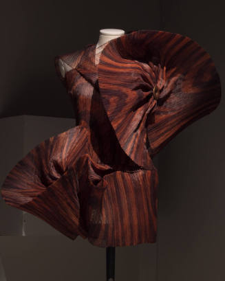 Brown and rust tie-dyed sleeveless mini dress of pleated fabric with oversize twisted panels on…
