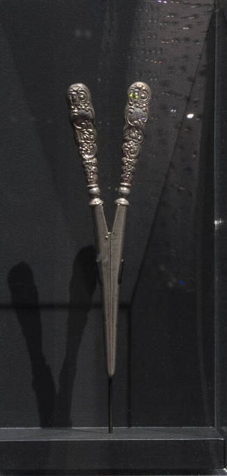 Silver glove stretcher with two tapering scroll patterned handles that meet at hinge and extend…