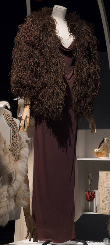 Brown jersey floor length gown with cowl neckline and brown feathered cape with elbow length sl…
