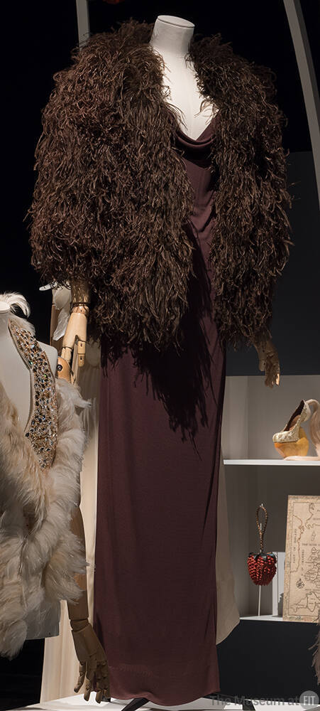 Brown jersey floor length gown with cowl neckline and brown feathered cape with elbow length sl…