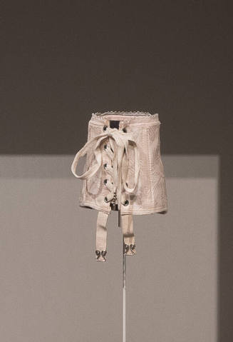 Pink patterned miniature sample corset with lacing through grommets and stretch garters at fron…