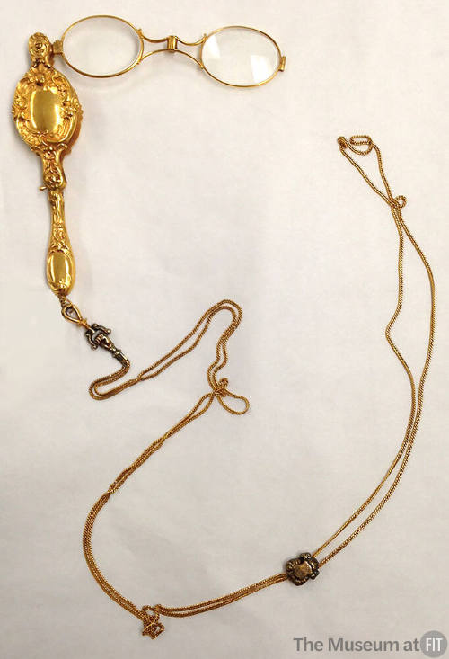 Gold lorgnette of eyeglasses with small oval frames attached to collapsible case with scrolling…