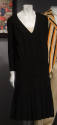 Black knee length dress with long sleeves, V-neck, scalloped bands along drop waist and knife p…