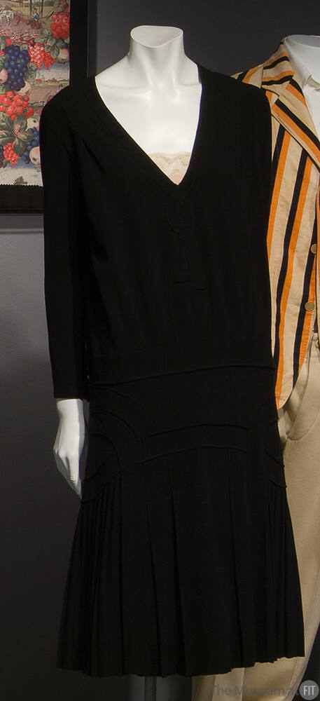 Black knee length dress with long sleeves, V-neck, scalloped bands along drop waist and knife p…