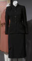Black suit with high shawl collar, four button center closure, tabs on left shoulder and right …
