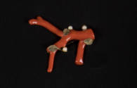 Brooch of a piece of red coral with three small pearls and gold leaves