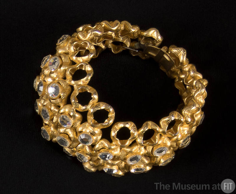 Gold cuff bracelet made of rows of circles, some empty and most encrusted with large rhinestone…