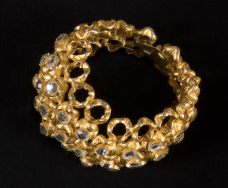Gold cuff bracelet made of rows of circles, some empty and most encrusted with large rhinestone…