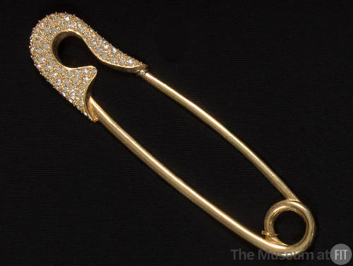 Gold ornament in the shape of a safety pin with rhinestone encrusted head