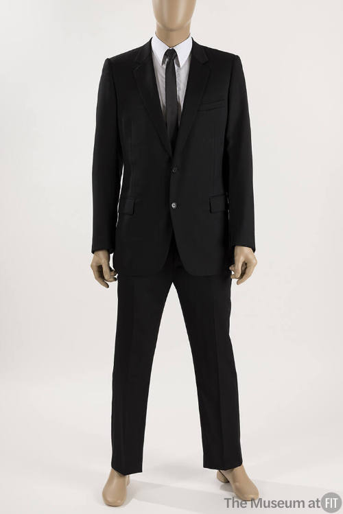 Man’s black two button suit with slim cut pants dressed with a white dress shirt and black tie